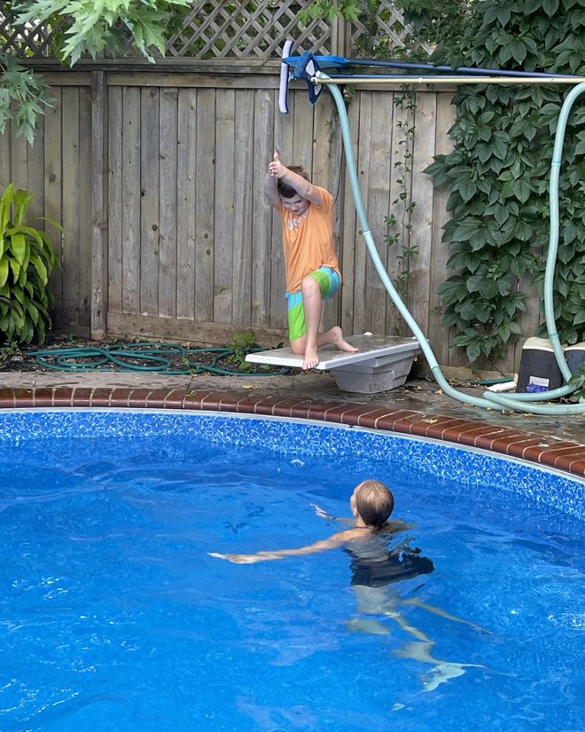 A young swimmer steadying himself on the diving board while an instructor waits in the water below