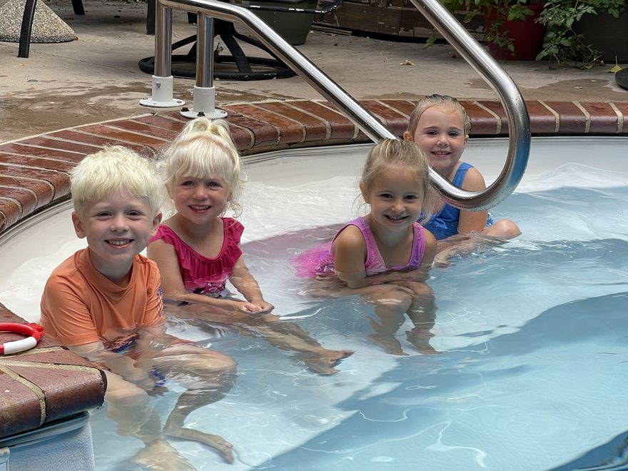 Four young swimmers grinning at the camera from the shallow steps of a backyard pool